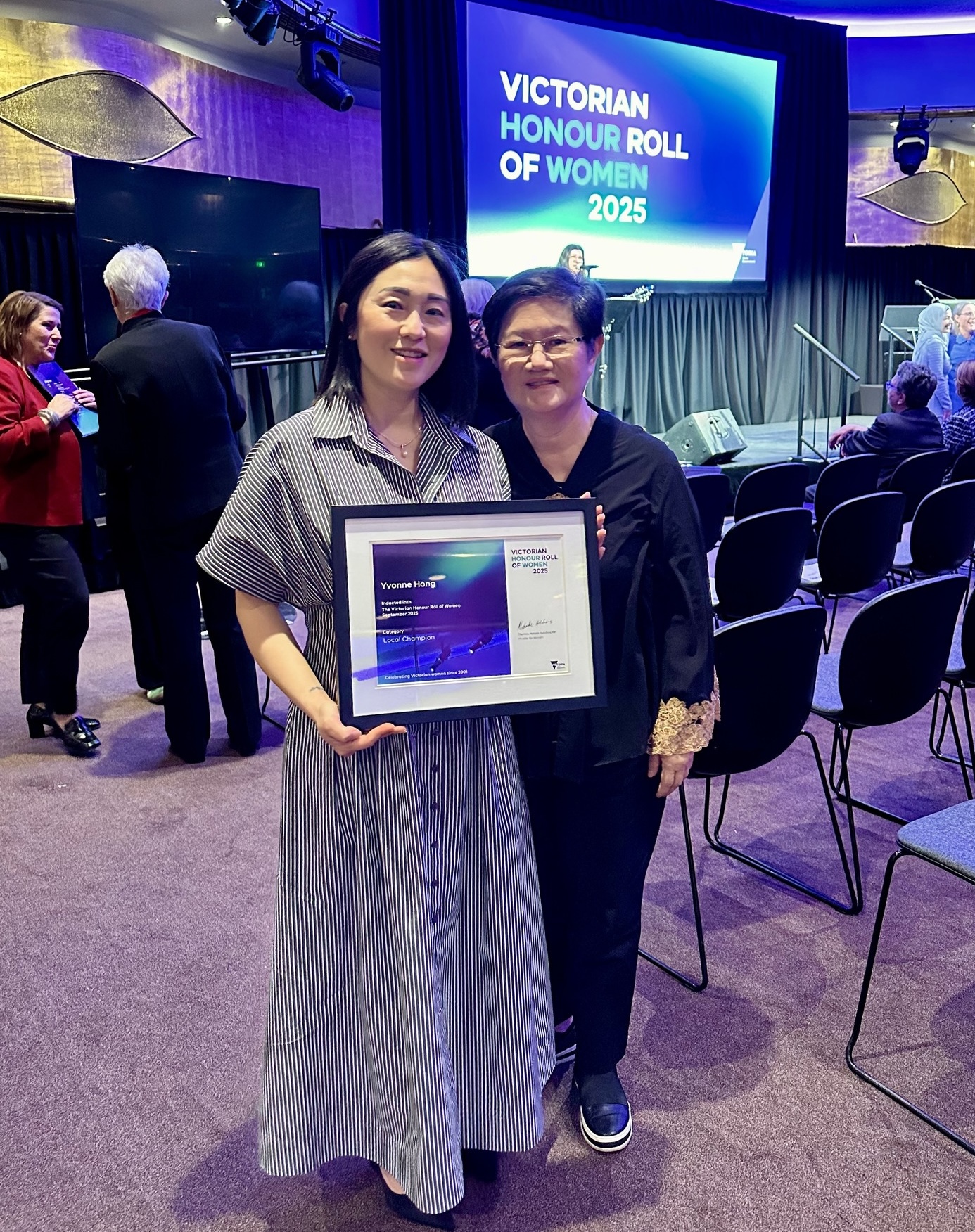 Yvonne Hong from Pets Of The Homeless stands with her mum proudly holding her Victorian Honour Roll of Women 2025 award at the ceremony venue, celebrating her recognition as a Local Champion.